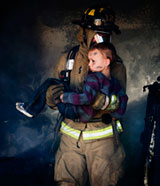 Image of a firefighter carrying a child from a smoke filled house